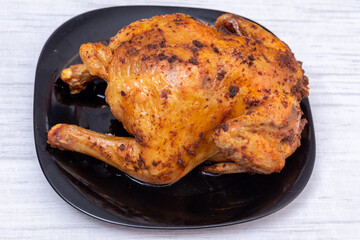 A whole fried chicken or turkey on a black plate on the table, top view. Chicken with a brown crispy crust.
