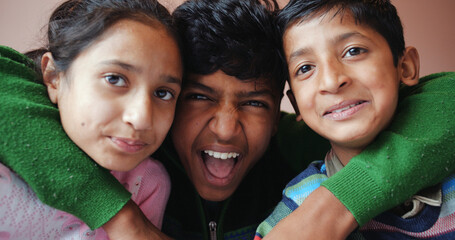 Closeup of three Indian siblings huddled together indoors