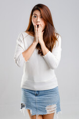 Portrait studio shot Asian young pretty happy female model in long sleeve shirt and short denim skirt stand hold hand index finger up at mouth say shh quiet sign look at camera on white background