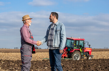 Happy farmer shaking hand with an owner at agricultural field.