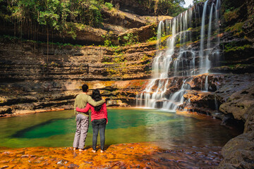 couple standing near waterfall flowing streams falling from mountain at morning from flat angle