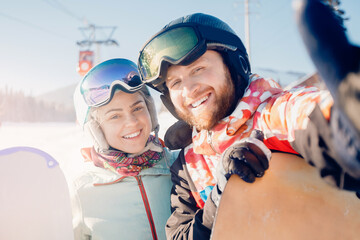Smiling couple taking selfie together background snowy mountain ski resort, sun light. Concept winter sports travel