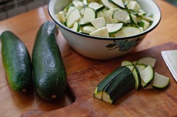 Bowl with chopped fresh green zucchini on the kitchen table. Cooking process. Green zucchini on a cutting board. Fresh sliced zucchini on cutting board, on wooden background.