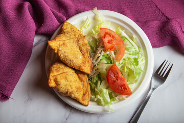 samosa on a plate with salad and tomatoes. horizontal view from above.