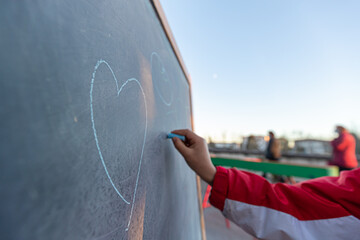 child hand drawing heart on outdoor blackboard