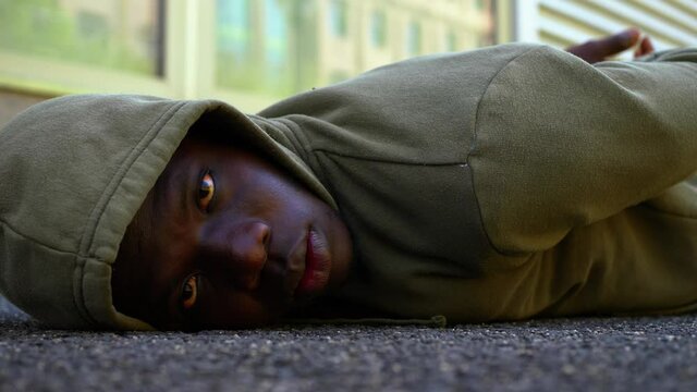 hooded black man lying on the ground stares at camera - protest symbol