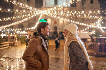 A young couple is having great moments under christmas lights of decorated square in the city. Christmas, New Year, holiday, love