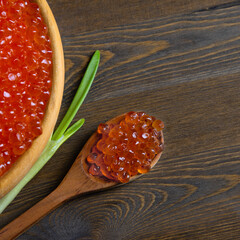 Red caviar in a wooden cup on a wooden background with a spoon.