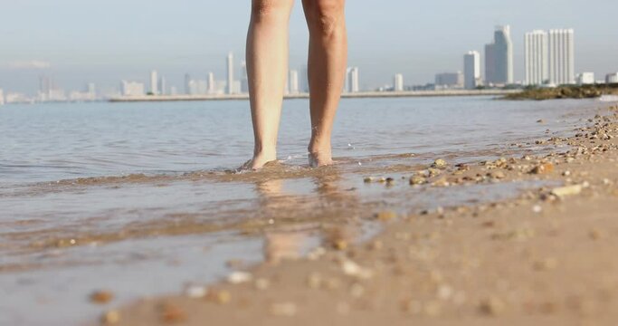 4K Video slow motion close up foot walking on the beach away from big city background. Concept for nature and vacation.