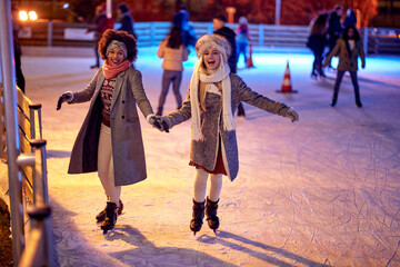 Beautiful gilfriends ice skating together; Winter joy concept - obrazy, fototapety, plakaty