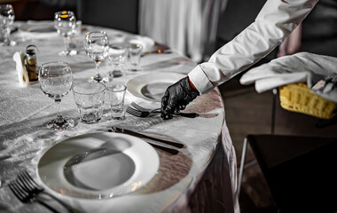 Waitress hand in gloves puts the knife and fork, table setting