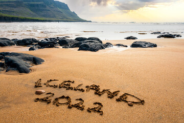 New year concept welcoming New Year 2022 written on a red sand beach with waves and red lava rocks on Iceland Ocean shore. 