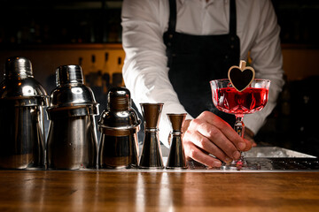 Bartender holding red tasty alcoholic cocktail in small glass decorated with little heart