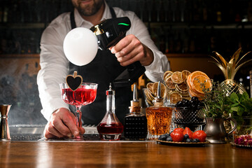 Bartender holding red tasty alcoholic cocktail and making smoke air bubble