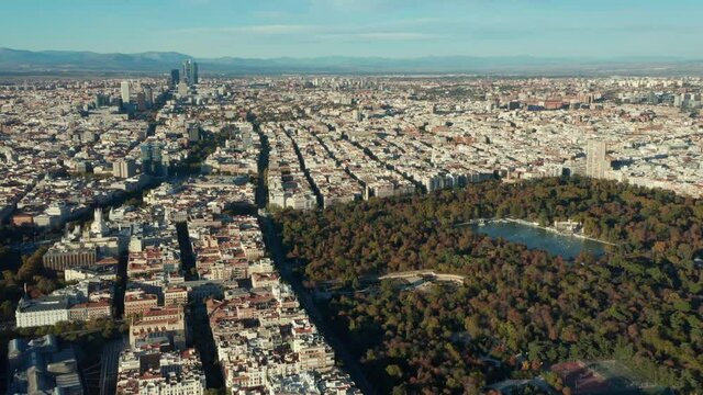 Aerial panoramic footage of large metropolis. Blocks of buildings separated by streets. Big green El Retiro park with sights and water surface.