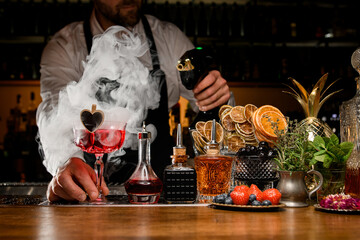 Bartender holding red tasty alcoholic cocktail and making smoke