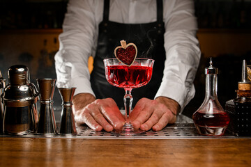 Hands of male bartender holding glass with red alcohol cocktail