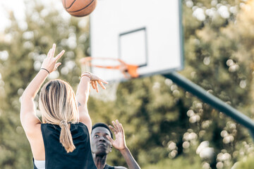 Selective focus on a woman shooting a ball at the basket while a man defends it