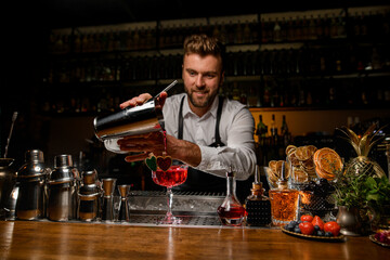 Smiling barman neatly pouring red fresh alcoholic drink into glass