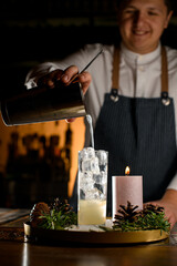 Young smiling bartender filling the cocktail glass with strong and fresh drink.