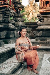 Portrait young woman with balinese face, wearing dress traditional Bali sarong in home temple. 