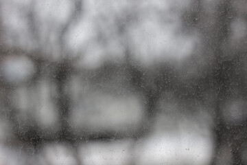 Dusty glass covered with dried rain drops. Snow falling outside the window on a cold winter day.
