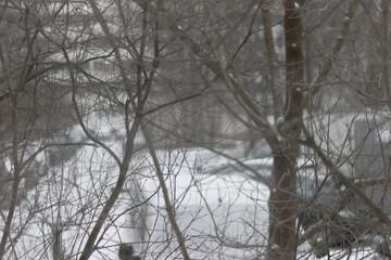 Dusty glass covered with dried rain drops. Snow falling outside the window on a cold winter day.