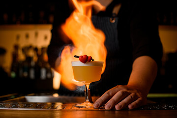 Bartender sets fire on glass with whiskey sour cocktail
