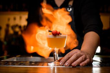 Barman sets fire on glass with whiskey sour cocktail