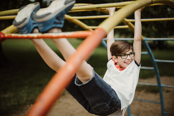 Fototapeta premium hanging around at climbing frame on playground looking happily to side and enjoy life while being satisfied with this waste of time of simple-minded childhood