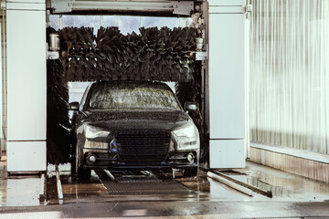 car wash automat with black vehicle drive through washing machine while cleaning and brushing the...