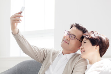 A middle-aged couple taking a selfie while sitting on the sofa in the living room at home