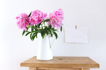 Desktop mock-up scene.Pink peony flowers in a white vase on an old wooden bench, table background. With copy space for greeting message. Spring flowers. Spring background.