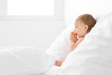 Profile portrait of baby girl with folded hands against her mouth