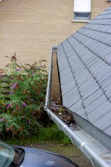 A portrait of a roof gutter full of water because it is clogged due to small branches and fallen...