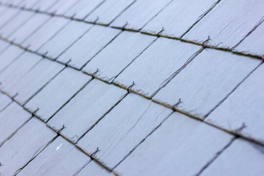 A close up portrait of a blue, black slate tile roof. The long lasting natural shingles are placed in a layered pattern and you can see the hooks keeping them in place.