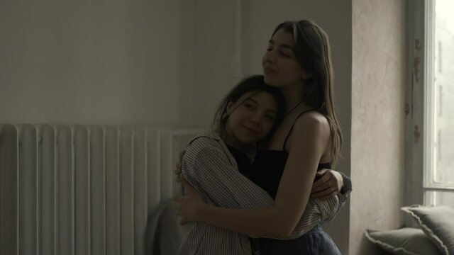 Two happy young women hug each other in a dark room. Woman of friendship, support and care. The women hug, smile and get excited. Filmed in cinematic style