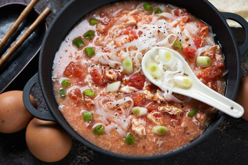 Middle close-up of chinese tomato egg-drop noodle soup in a cast-iron pan, horizontal shot