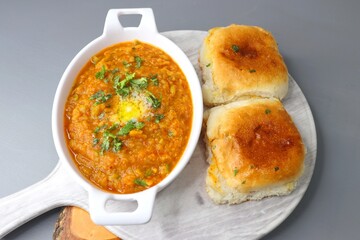 Indian Mumbai Street style Pav Bhaji, garnished with peas, raw onions, coriander and Butter. Spicy thick curry made of out mixed vegetables, served with pav over black background with copy space.