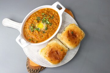 Indian Mumbai Street style Pav Bhaji, garnished with peas, raw onions, coriander and Butter. Spicy thick curry made of out mixed vegetables, served with pav over black background with copy space.