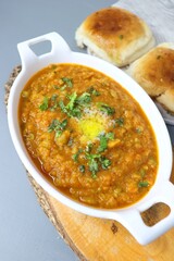 Indian Mumbai Street style Pav Bhaji, garnished with peas, raw onions, coriander and Butter. Spicy thick curry made of out mixed vegetables, served with pav over black background with copy space.