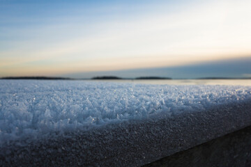 Snow frost abstract winter background close-up bokeh, Cold season rime ice crystals on wooden embankment of lake Malaren, evening sky, Vasteras, Sweden