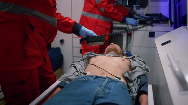 Emergency medical doctors using heart defibrillator on patient in ambulance car