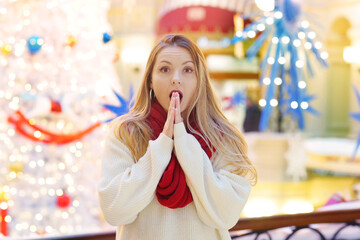 happy blond girl in red scarf with frightened expression and gesture close up portrait on decorated Christmas city mall background