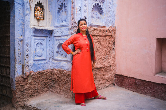 Beautiful Indian female model at blue district of the old city in Jodhpur, Rajasthan, India. Hindu girl with long hair, tilak and traditional Indian red kurta next to a Ganesh statue. 