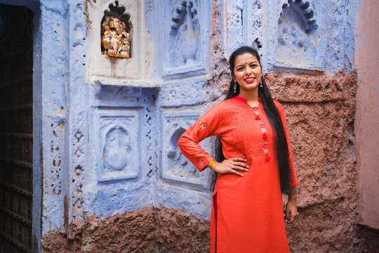 Beautiful Indian female model at blue district of the old city in Jodhpur, Rajasthan, India. Hindu girl with long hair, tilak and traditional Indian red kurta next to a Ganesh statue. 