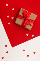 gift box in craft packaging and with a red ribbon on a red and white background with hearts in a vertical format