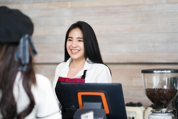 Asian caucasian waitress, a small company owner, a barista, and a bartender in a black apron smiling and looking at customer at the bar counter in a cafe shop