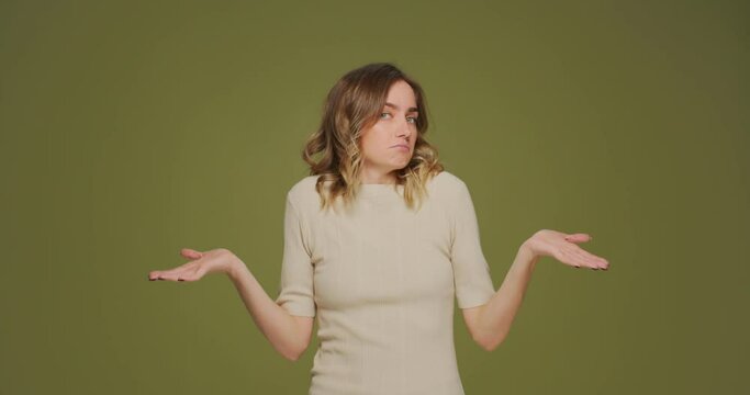 Confused puzzled young woman being in perplexity shrugged shoulders on green studio background. I dont know 