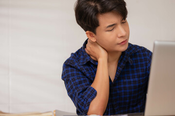 Working online at home on a laptop desk has given an Asian businessman a headache and fatigue.